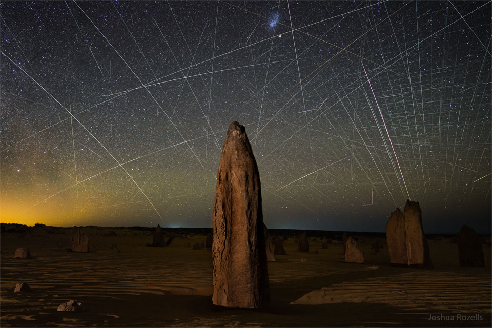 Opisywane zdjęcie pokazuje iglice skalne, znane jako Pinakle, występujące
w Australii. Za nimi jest niebo wypełnione śladami satelitów, w tym wiele z konstelacji
Starlinków na niskiej orbicie okołoziemskiej. Zobacz opis. Po kliknięciu
obrazka załaduje się wersja o największej dostępnej
rozdzielczości.