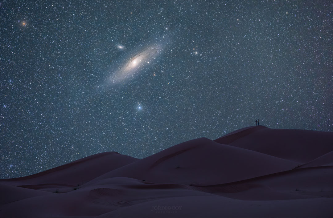 Opisywane zdjęcie pokazuje zbliżenie na Galaktykę Andromedy
nad wydmami Sahary. Na szczycie jednej z wydm można dostrzec dwoje ludzi.
Zobacz opis. Po kliknięciu obrazka załaduje się wersja
 o największej dostępnej rozdzielczości.