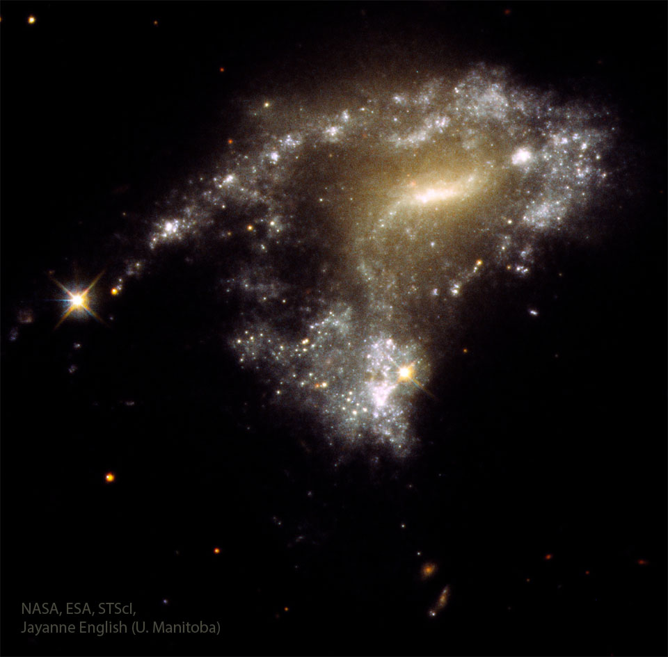 A distorted galaxy is shown with a string of
stars trailing off on the left.
Więcej szczegółowych informacji w opisie poniżej.