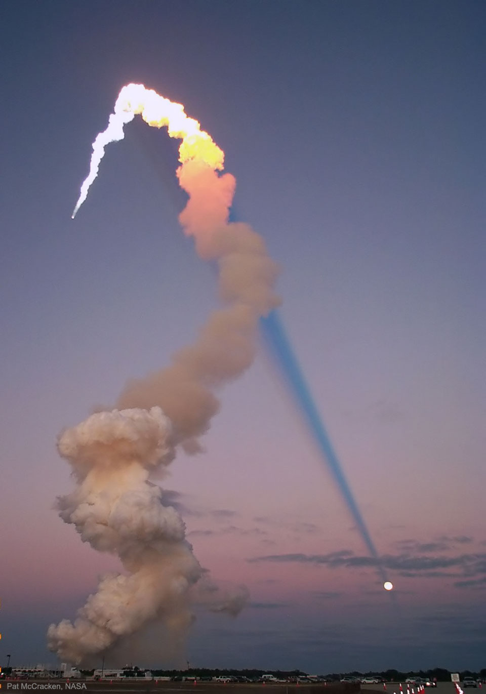 The long plume of a launching rocket is seen on
the left side of the image. The upper part of the plume
is bright, while the lower part is smokey brown. The bright
part of the plume is illuminated by the Sun and casts
a long and dark shadow corridor across the image. The
shadow appears to end on a Full Moon. 
Więcej szczegółowych informacji w opisie poniżej.