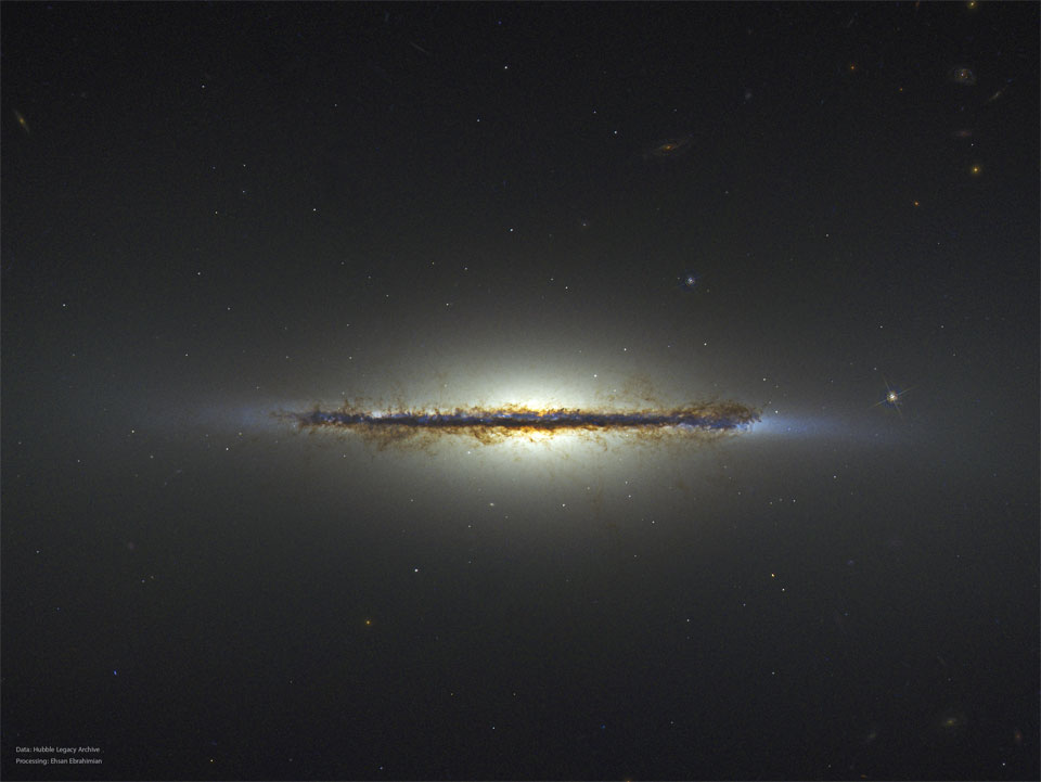 A starfield is shown with an unusual horizontal line 
segment running throug the middle. The segment is an
edge-on galaxy and many brown dust filaments are visible.
Więcej szczegółowych informacji w opisie poniżej.